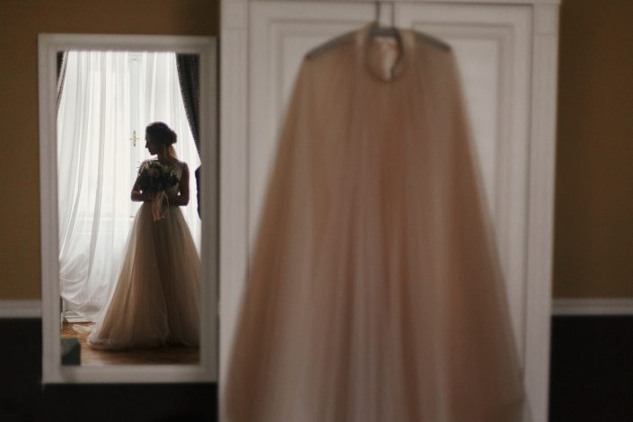 Gorgeous bride silhouette standing at window light, looking in stylish wedding dress, in the morning. Creative image. Bride and her beautiful wedding gown. Woman getting ready